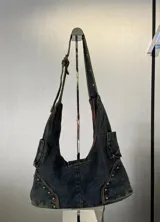Cartera bandolera de denim azul con detalles de tachas y hebilla metálica.