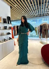 Vestido largo de fiesta color verde oscuro, con mangas acampanadas y falda con volados en cascada. Incluye clutch plateado.