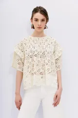 Blusa blanca de broderie con escote redondo, mangas cortas con volados en sisa y detalle de alforzas en el canesú.