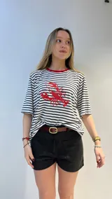 Remera oversize a rayas horizontales blancas y negras con cuello rojo y estampado de langosta roja. Corte holgado y mangas cortas.