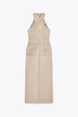 Vestido midi color beige con cuello halter cruzado, cinturón con hebilla y bolsillos tipo parche.