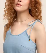 Vestido corto de jeans celeste, con breteles finos con lazos, escote en U, espalda descubierta y falda de tres niveles con volados.