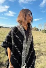 Ruana tejida a mano en telar, confeccionada en lana Merino color negro con detalles en blanco y flecos blancos.