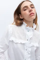 Camisa blanca de algodón con bordado calado, cuello alto con volados y cierre frontal con botones.
