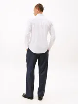 Camisa blanca de corte slim, confeccionada en tejido dobby de algodón elástico con textura sutil. Presenta cuello con botones, puños redondeados con botón y el logo de Tommy Hilfiger bordado en el pecho.