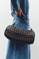 Bolso de hombro con cuerpo trenzado en color negro y marrón. Tiene detalle metálicos circulares en los laterales, asa de hombro, bolsillo interior con cremallera y cierre mediante solapa y cremallera.