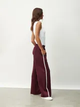 Pantalón deportivo color borgoña, de corte ancho y cintura elástica. Presenta una franja blanca vertical a lo largo de la pierna.