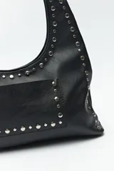 Cartera negra tipo hobo de cuero sintético con apliques de tachas metálicas plateadas en el frente y los bordes.