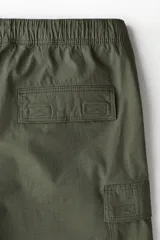 Short cargo color verde militar, de corte regular, con cintura elástica ajustable con cordón, bolsillos laterales, bolsillos cargo con solapa y cierre autoadherente en las piernas y bolsillos traseros con solapa y cierre autoadherente.