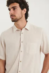 Camisa sport de manga corta color verde oliva, línea premium, con cuello clásico, cierre frontal con botones de coco y bolsillo de parche en el pecho. Confeccionada en lino y algodón.