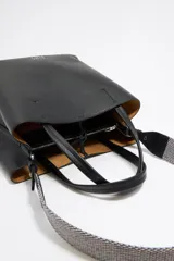 Bolso tote negro de cuero vacuno con doble asa corta y correa de tela extraíble. Interior con tres compartimentos y bolsillo con cremallera. Logo metálico de la marca en el frente.