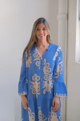 Vestido largo celeste con estampado floral en beige, corte evasé, cuello camisero, mangas largas con volados y falda escalonada.