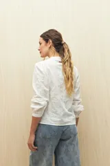 Camisa color beige con bordado floral blanco en toda la superficie. Presenta cuello mao, escote en V y abotonadura frontal, con mangas largas terminadas en puño angosto.