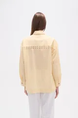 Camisa de algodón blanca, de corte ancho, con botones de madera y detalles de encaje calado en el frente, mangas y ruedo. Tiene cuello camisero y manga larga.