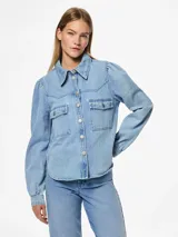 Camisa de denim celeste de algodón, de corte regular, con cuello clásico, mangas largas con puños abotonados, bolsillos con solapa abotonada en el pecho y cierre frontal con botones.