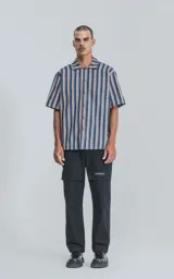 Camisa de manga corta con cuello abierto y calce oversize, confeccionada en sarga liviana a rayas verticales en tonos azul, amarillo y rojo.