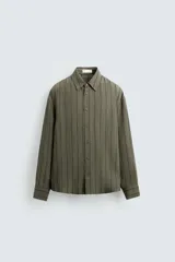 Camisa verde militar con rayas verticales negras, de corte regular fit, cuello solapa, manga larga con puños abotonados y cierre frontal con botones.