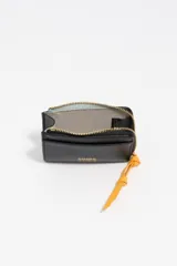 Monedero pequeño de estructura rígida, color negro, con cierre de cremallera y tirador de tejido amarillo mostaza. Presenta un bolsillo exterior frontal y el logo de la marca grabado en dorado.