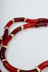 Collar corto de cuentas tubulares rojas y borgoña alternadas con detalles dorados.