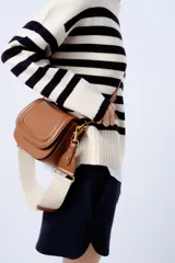 Bolso bandolera color marrón con solapa y correa ancha de tela color crudo.