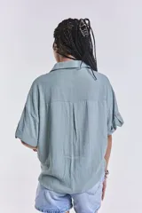 Camisa verde agua con cuello clásico, cierre frontal con botones, mangas cortas con dobladillo y dos bolsillos de parche en el pecho.