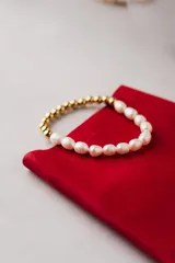 Pulsera elástica con cuentas de perlas blancas y cuentas doradas.
