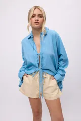 Camisa blanca de lino y algodón, con cuello clásico, cierre frontal con lazos y mangas largas abullonadas con puños ajustables con lazos.