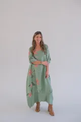 Vestido largo verde con estampado floral en tonos rosados y blancos, mangas 3/4 con ajuste de botón y ruedo irregular.