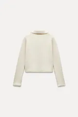 Chaqueta color crudo de tejido de punto con cuello solapa y manga larga. Tiene bolsillos de parche delanteros y cierre cruzado con doble botonadura.