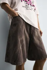 Bermuda de jean color marrón oscuro con efecto lavado, corte amplio, cinco bolsillos y cierre frontal con cremallera y botón.