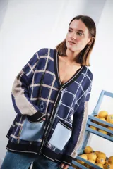 Cardigan oversized de tejido jacquard color crema con diseño de cuadrados en marrón y detalles bordados. Tiene cuello en V, cierre con botones, mangas largas y bolsillos frontales.