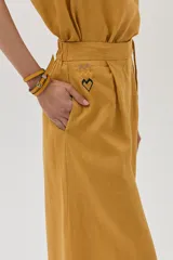 Pantalón de lino color mostaza, de corte palazzo, con lazo en la cintura, pinzas en el frente y bolsillos laterales.