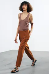Pantalón color marrón confeccionado en hilatura con mezcla de lyocell y algodón. Tiro medio, cintura con trabillas, bolsillos laterales, pinzas en delantero y raya planchada. Cierre frontal con cremallera, botón y ganchos metálicos.