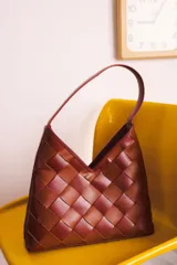 Cartera de cuero trenzado a mano, con forro interior y asa corta. Diseño con patrón de tablero en tonos marrones.