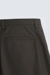 Pantalón de vestir negro de corte recto, confeccionado en tejido de algodón con acabado ligeramente encerado. Cuenta con bolsillos laterales y traseros de vivo. El cierre frontal es con cremallera y gancho metálico oculto.