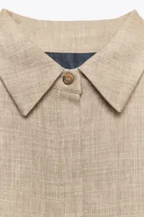 Chaqueta bomber color beige con cuello solapa y manga larga. Tiene bolsillos delanteros y bajo ajustable con cordones. Cierre frontal con botones ocultos.