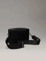 Bandolera negra Calvin Klein Must de piel sintética granulada, con correa ajustable jacquard con logo, cierre de cremallera, bolsillo interior y logo de metal plateado brillante en la parte delantera.