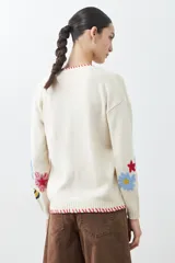 Cárdigan color crema con botones, ribete rojo y bordados de flores y mariposas en las mangas.