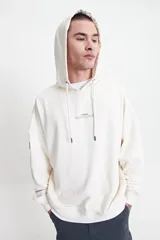 Canguro de felpa color crema, con capucha ajustable, puños y logo estampado en el pecho.