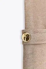 Pantalón de sarga color beige, de tiro medio con cintura elástica en la espalda, bolsillos laterales de plastrón con botón metálico y pierna ancha.