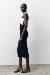 Vestido midi negro de tejido elástico, con escote recto y cuello halter. Presenta un lazo blanco a contraste en el delantero con aplicación de perlas y espalda descubierta.
