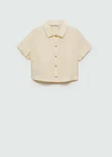 Camisa color crema de lino, con cuello camisero, manga corta con dobladillo y cierre frontal con botones.
