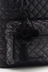Mochila negra matelassé con correa ajustable y manijas para llevar al hombro. Tiene cierre de cremallera, accesorio colgante decorativo, bolsillo interno y espacio para laptop.