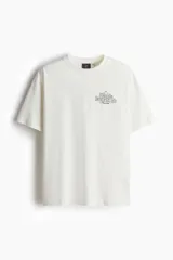 Remera blanca de corte holgado con cuello redondo y estampado de Snoopy con la leyenda "Peanuts Racquet Club" en el pecho.