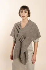 Chal asimétrico de lana color gris claro, con cortes en los hombros y doble ojal de fieltro para mantener el cruce. Terminación pespunteada y al corte.