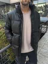 Campera puffer negra de símil cuero, con cuello alto y cierre frontal con cremallera.