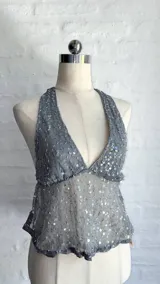 Top halter gris claro, ajustado al cuerpo, con escote pronunciado en V y cubierto de lentejuelas plateadas. El tejido es semitransparente.