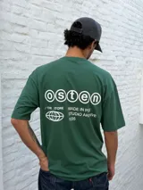 Remera oversize color verde bosque con estampado minimalista en blanco en el pecho: un globo terráqueo estilizado y el texto "STUDIO ARCHIVE".