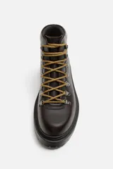 Bota de cuero color marrón oscuro con cordones amarillos, estilo trekking, con suela de goma con volumen.