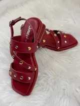 Sandalias rojas de cuero con tiras cruzadas y detalle de tachas plateadas y doradas.
